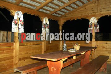 Imagine cu foisorul din lemn cu aspect traditional maramuresean cu mese din lemn, in curtea pensiunii Narcisa din Botiza