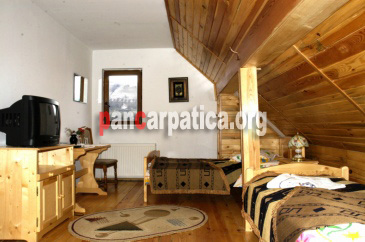 Imagine cu mansarda pensiunii Vila Maria -Simon cu mese, scaune din lemn si televizor