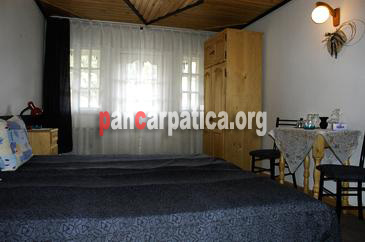 Imagine interior a unui dormitor cu pat mare si confortabil, masa si scaune din lemn la pensiunea Orizont din Farcasa