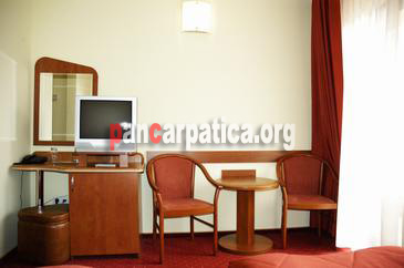 Imagine interior in pensiunea Vanatorul-Vatra Dornei cu masa din lemn, scaun comod, canapea si televizor cu canale tv