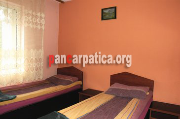Imagine a unui dormitor spatios cu 2 paturi simple comode din pensiunea Fratii Mihali-Borsa